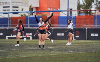 Para pemain wanita merayakan setelah mencetak gol dalam pertandingan flag football di lapangan terbuka yang semarak.