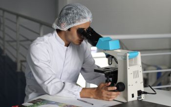 Ilmuwan memakai jas laboratorium menggunakan mikroskop untuk melakukan penelitian, fokus pada perbaikan dalam layanan kesehatan.