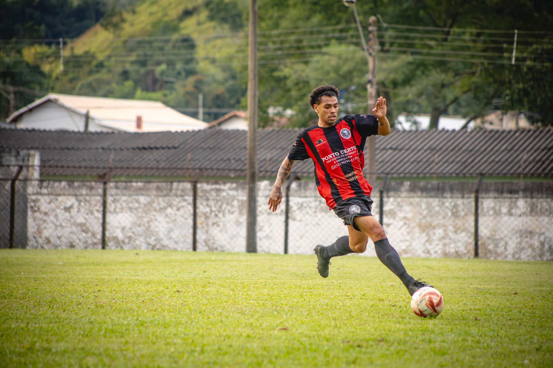 Pemain sepak bola dengan keterampilan menendang bola di lapangan rumput selama pertandingan.