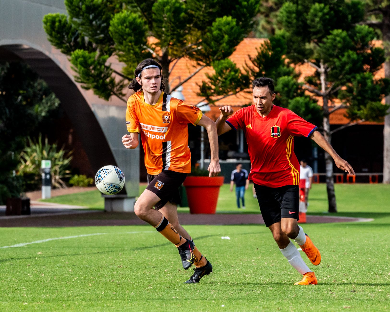 Dua pemain sepak bola sedang bertanding di luar ruangan, menunjukkan semangat olahraga kompetitif di hari yang cerah.