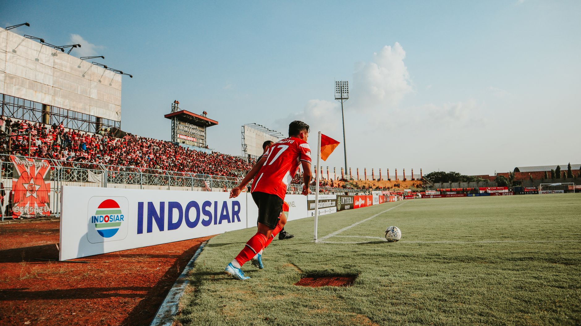 Seorang pemain sepak bola melakukan tendangan sudut di stadion Indonesia yang ramai dan dipenuhi penggemar.