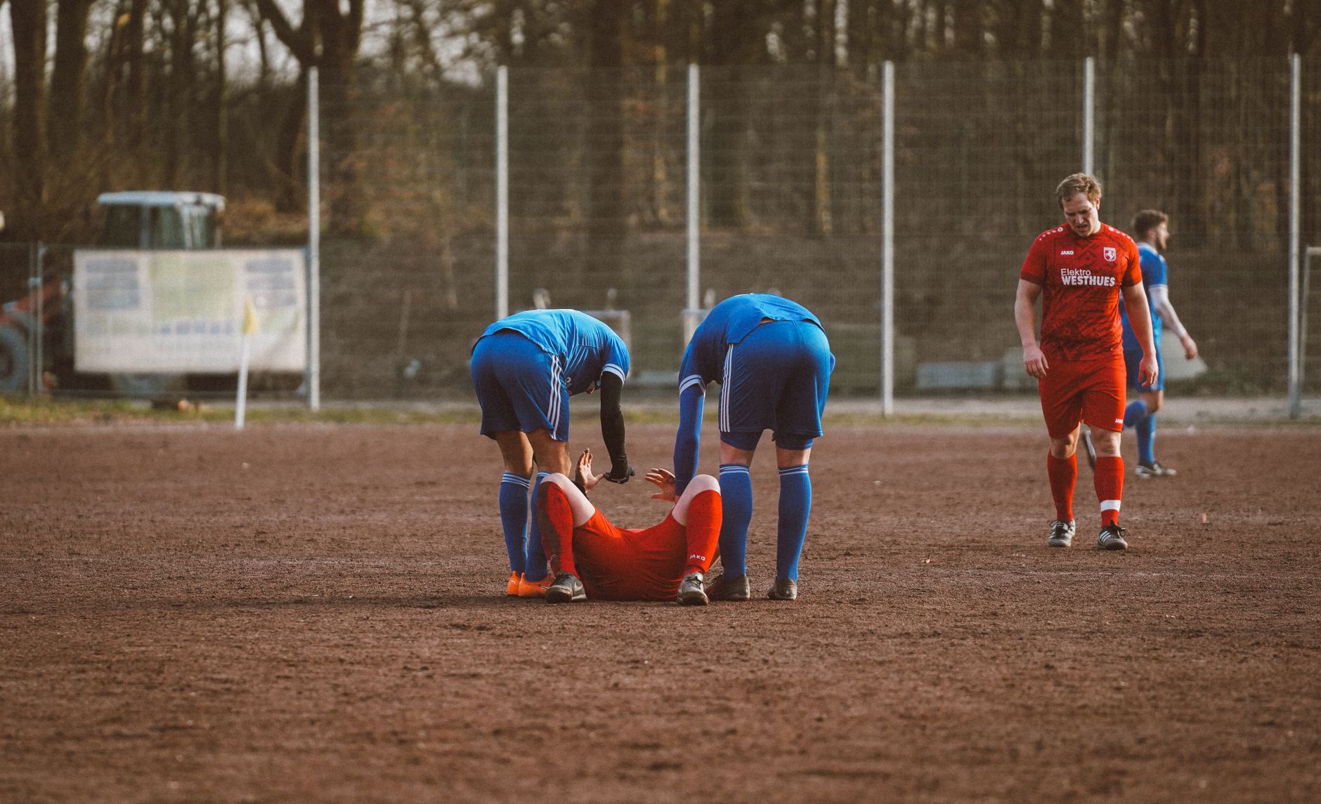 Pemain di lapangan sepak bola membantu rekan setimnya yang cedera, menyoroti kerja sama tim dan sportivitas.