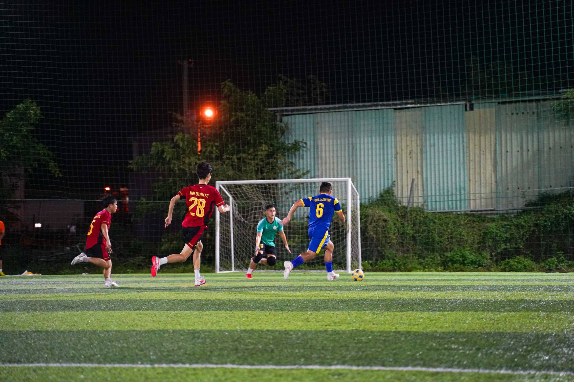Pemain sepak bola muda sedang beraksi di lapangan yang diterangi di malam hari, menunjukkan kerja tim dan energi.
