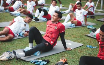 Pemain sepak bola yang melakukan latihan peregangan di lapangan berumput, Jakarta.