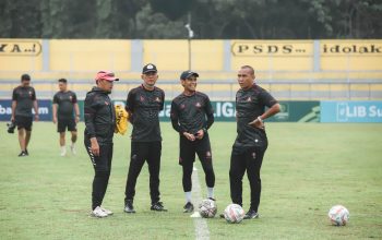 Sekelompok pelatih Indonesia berdiskusi di lapangan sepak bola di siang hari.