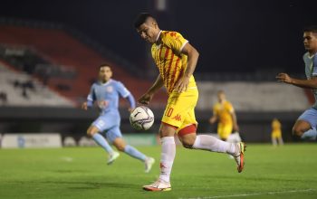 Pemain sepak bola dalam aksi selama pertandingan malam kompetitif di lapangan sepak bola yang diterangi dengan baik.