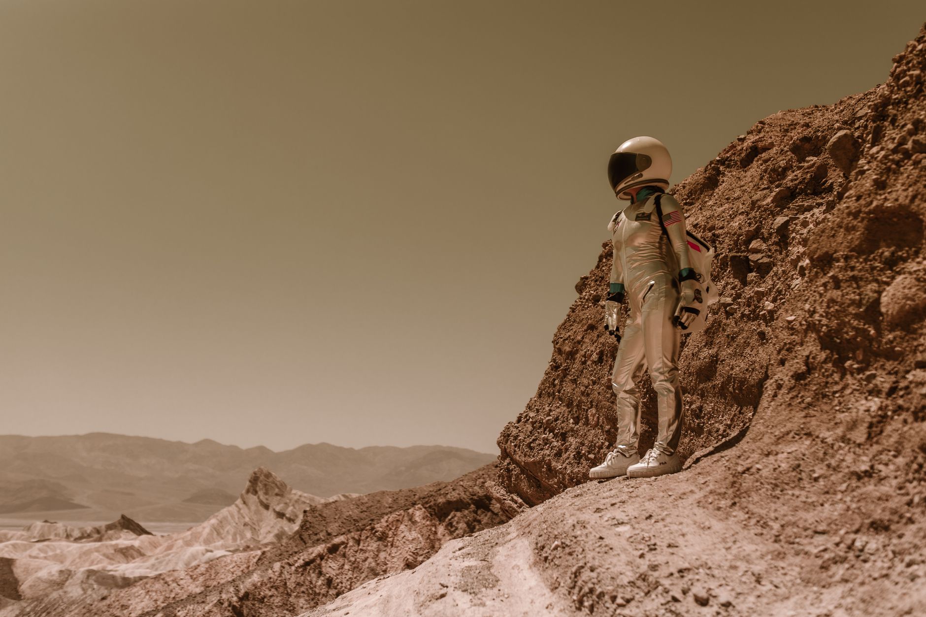 Seorang astronot tunggal dalam pakaian luar angkasa berdiri di medan berbatu yang keras menyerupai planet asing.