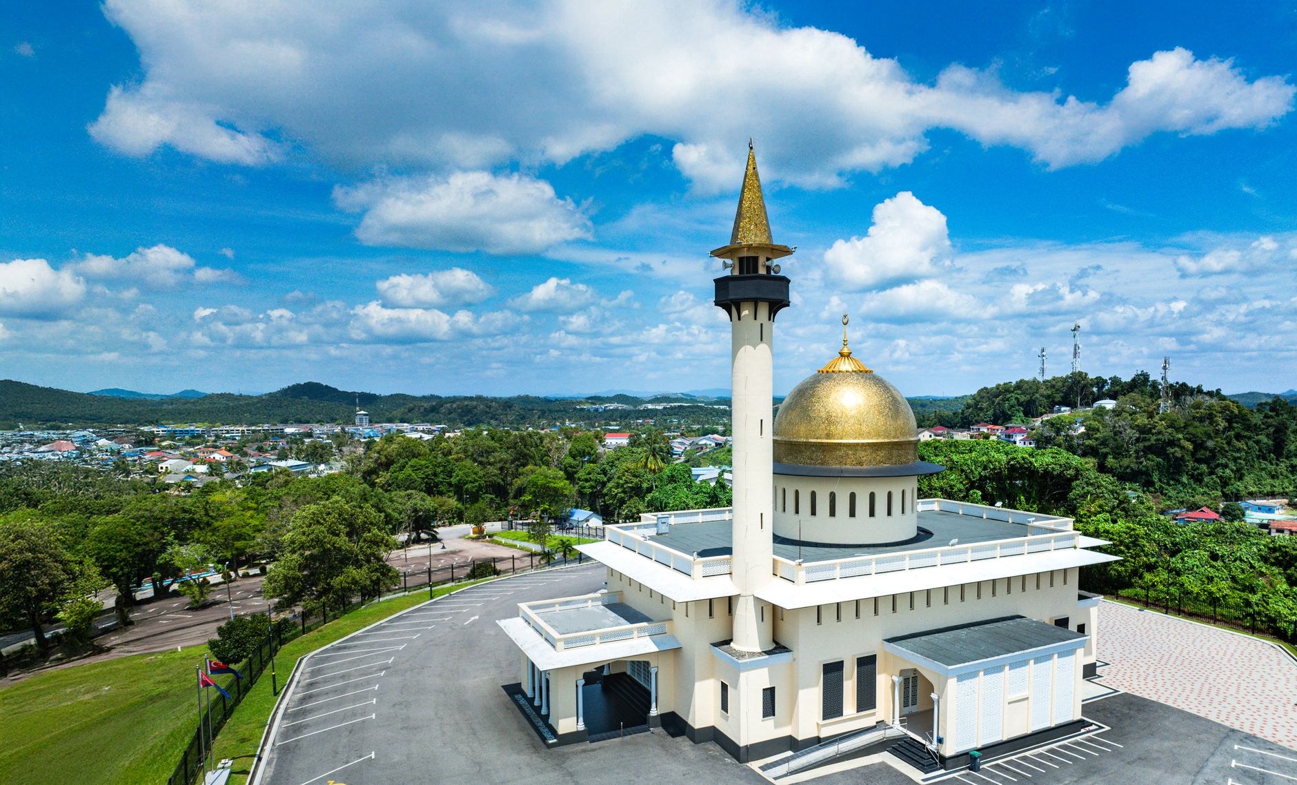 Pemandangan udara menakjubkan Masjid Jamek Bandar Mersing di Johor, menampilkan kubah emas dan menara di latar belakang langit biru yang cerah.