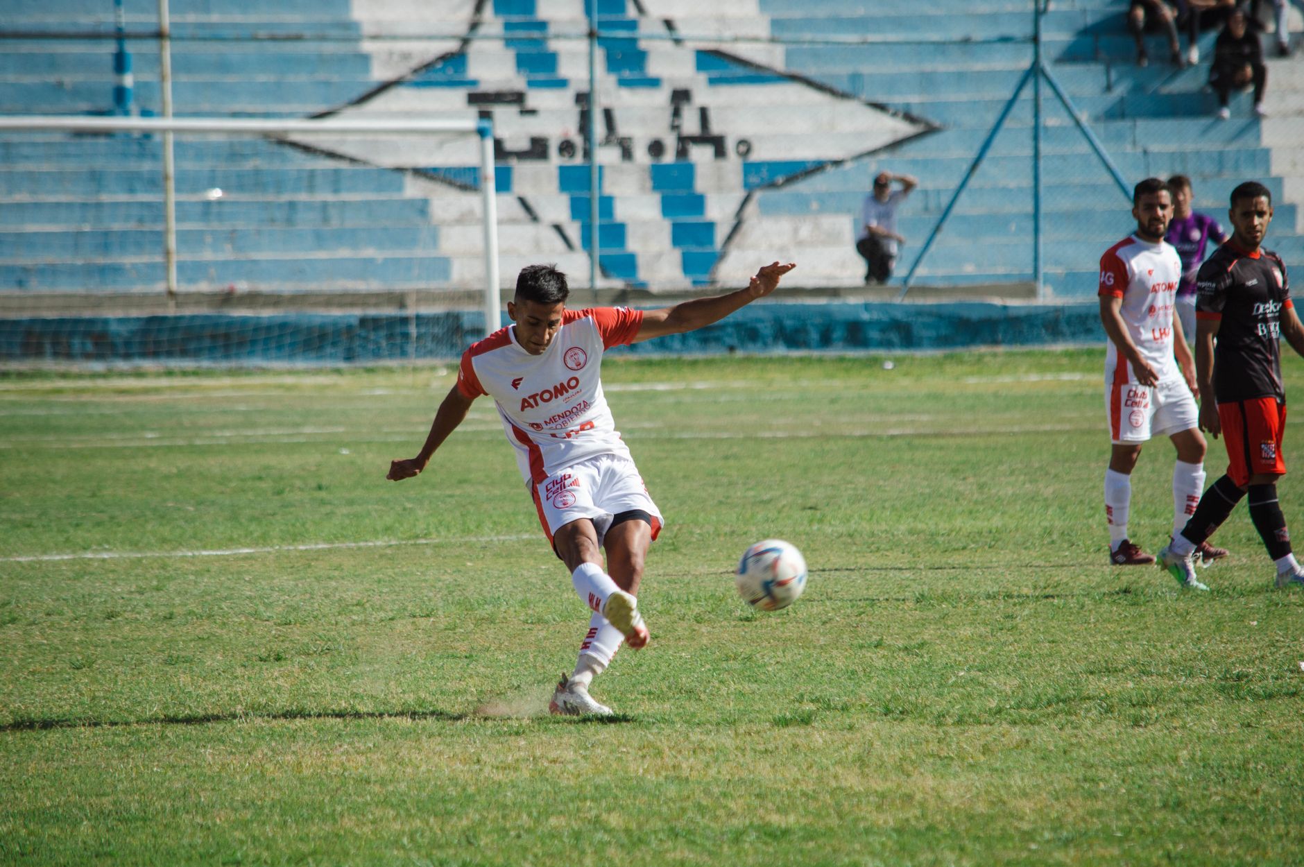 Momen dinamis dalam pertandingan sepak bola di Mendoza, Argentina. Pemain bergerak di lapangan rumput.
