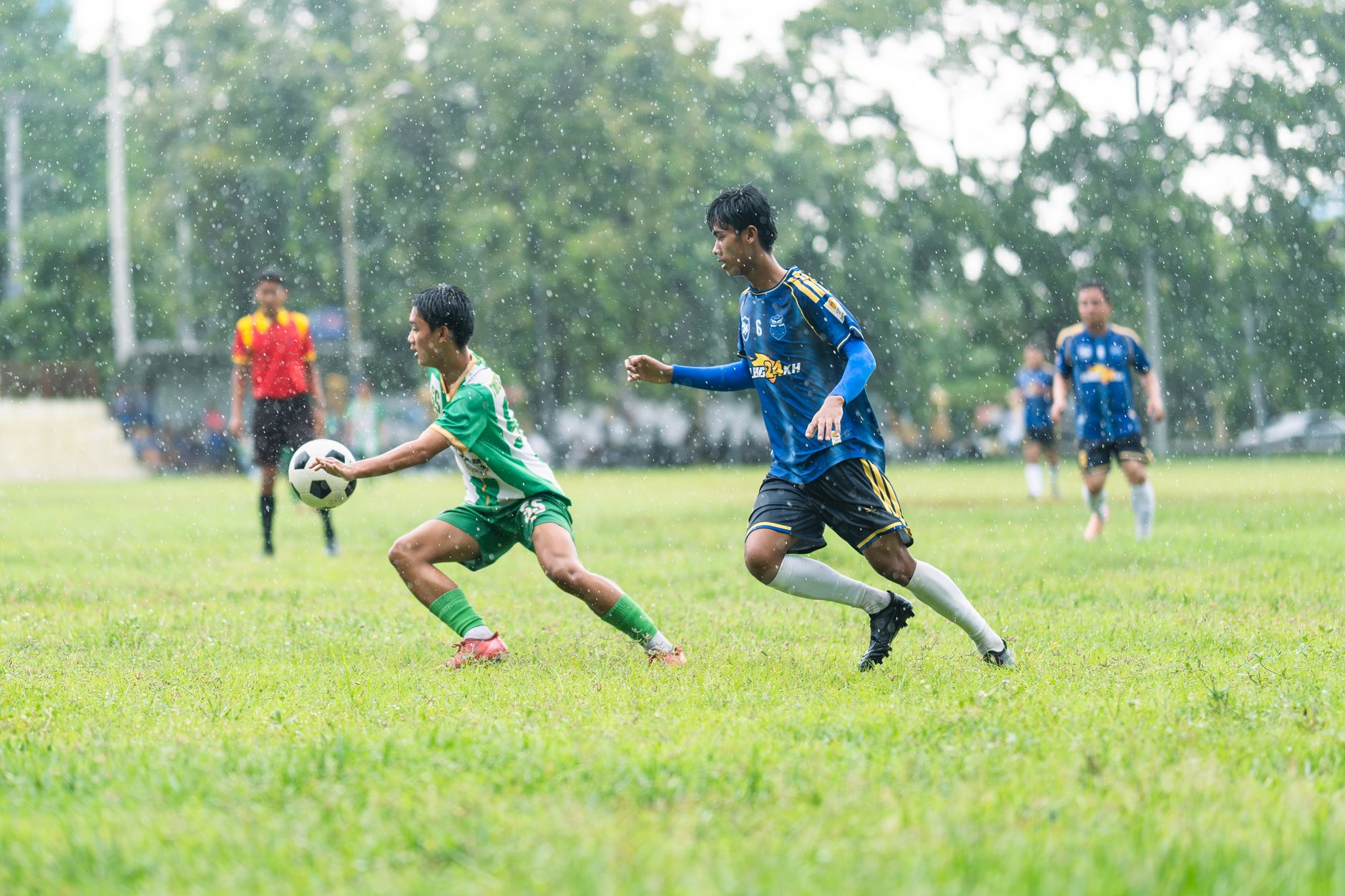 Para pemain dalam pertandingan sepak bola di tengah hujan menunjukkan tekad dan kerja sama tim.