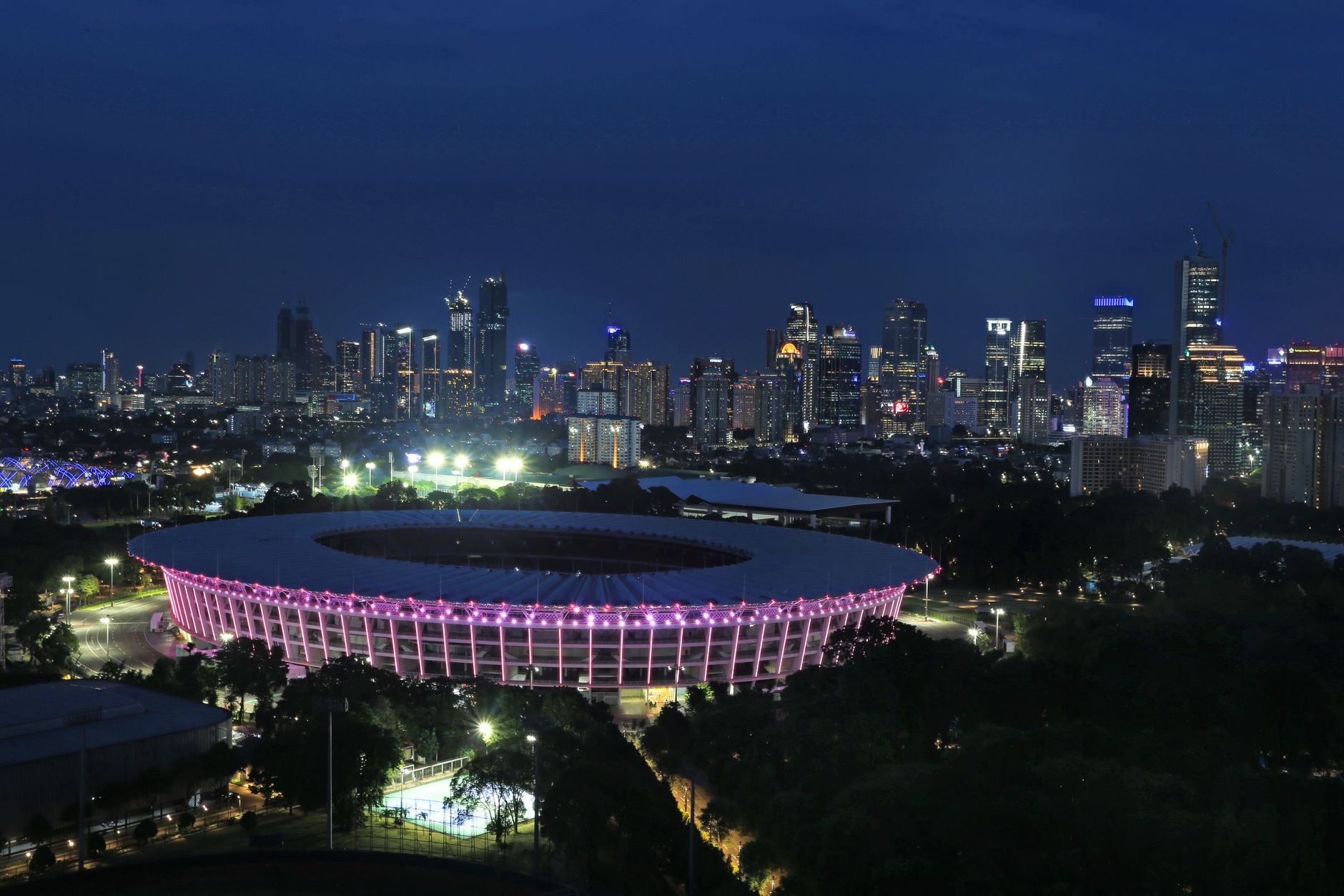 Pemandangan cakrawala malam Jakarta yang menakjubkan dengan Stadion Gelora Bung Karno yang diterangi lampu di bagian depan.