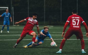 Pengambilan gambar dinamis pemain sepak bola saat beraksi selama pertandingan kompetitif di lapangan rumput.
