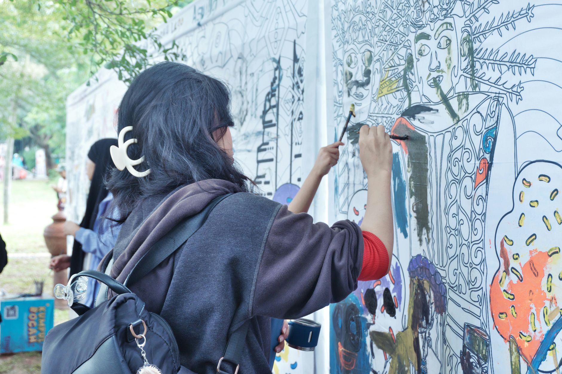 Seniman perempuan melukis mural berwarna-warni di Jakarta, Indonesia di siang hari.