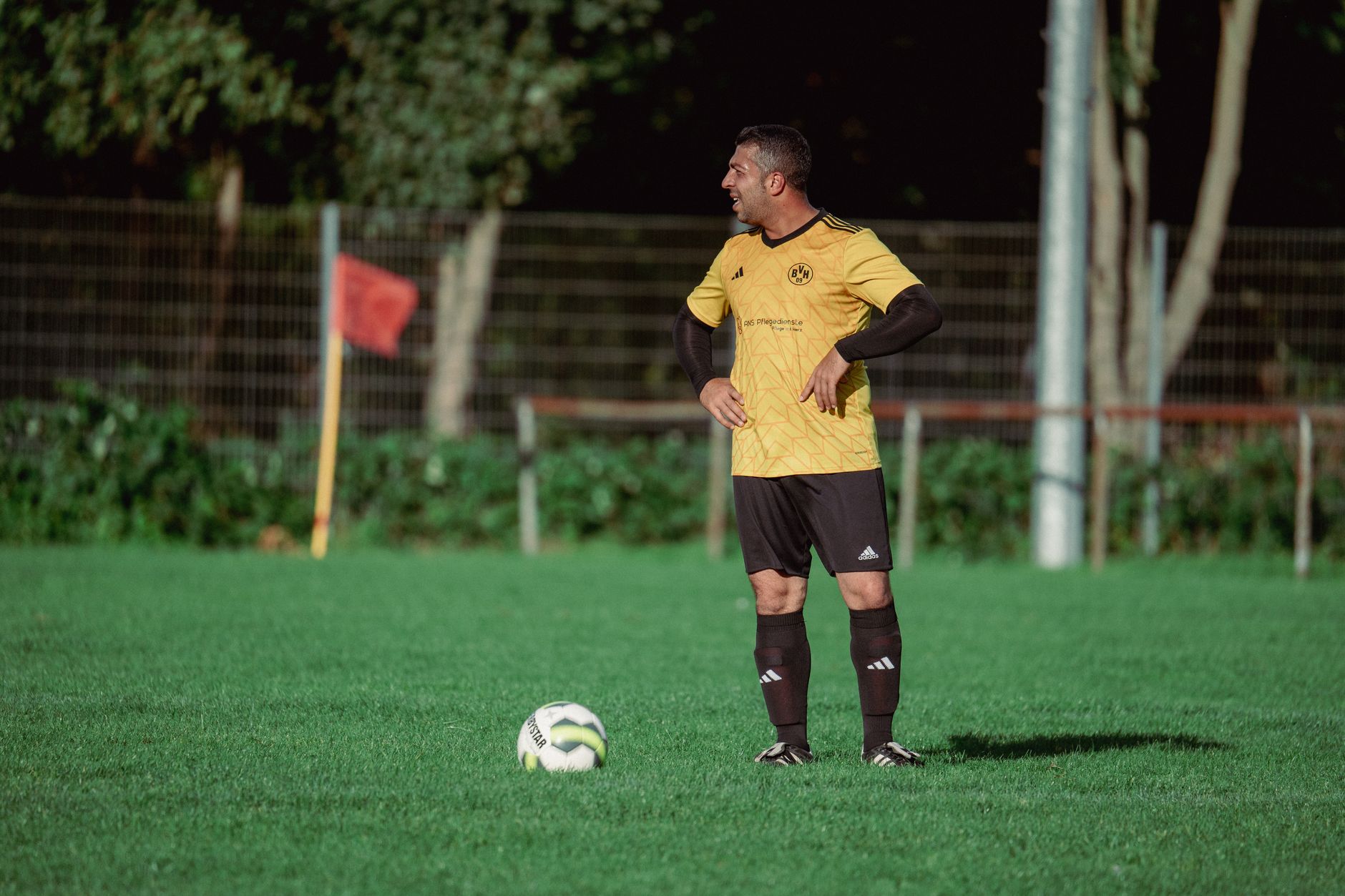 Pemain sepak bola dewasa di lapangan luar ruangan yang cerah, bersiap untuk bermain.