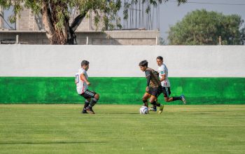Pertandingan sepak bola kompetitif yang menampilkan pria muda beraksi di lapangan luar ruangan yang cerah.