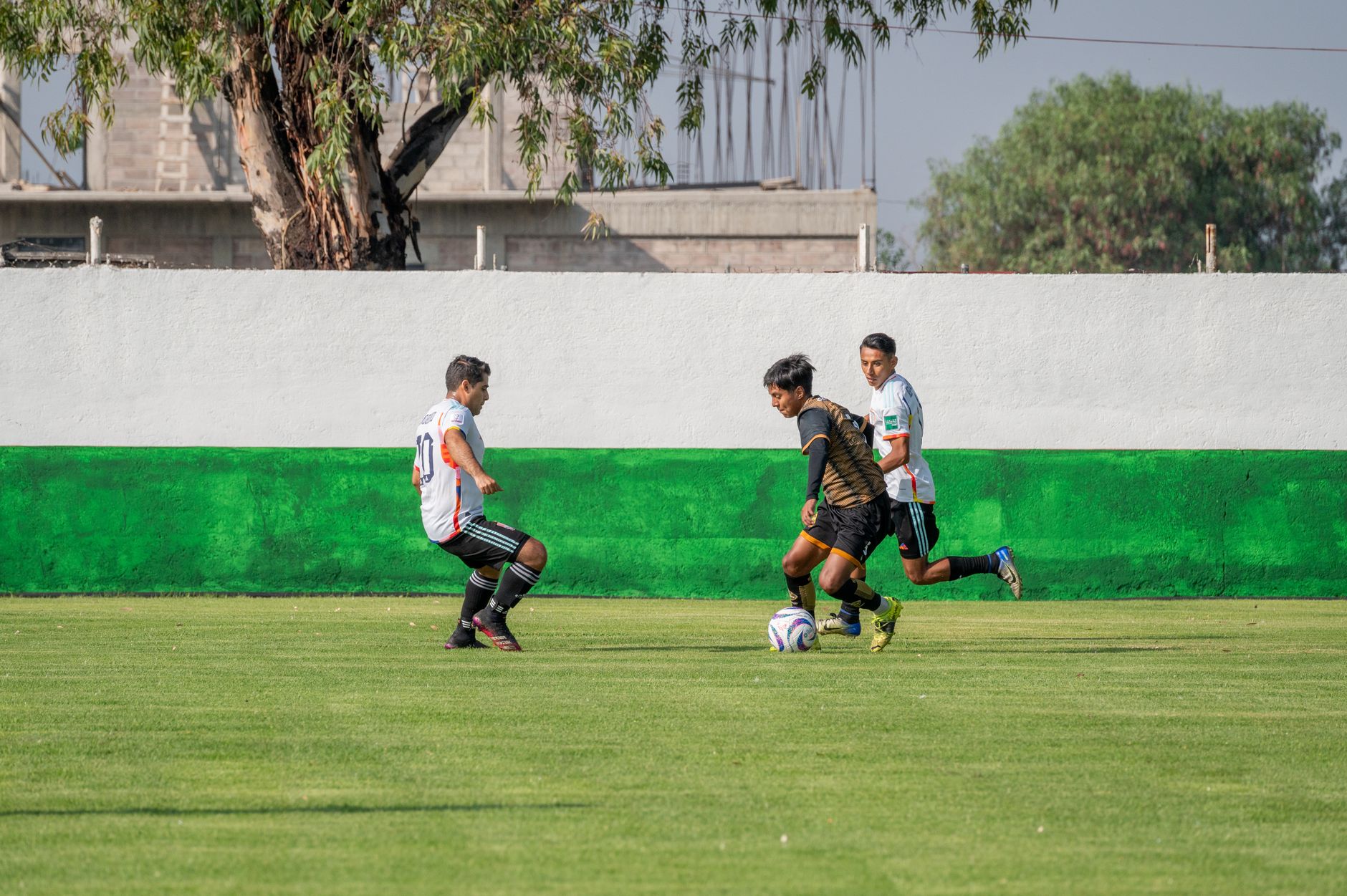 Pertandingan sepak bola kompetitif yang menampilkan pria muda beraksi di lapangan luar ruangan yang cerah.