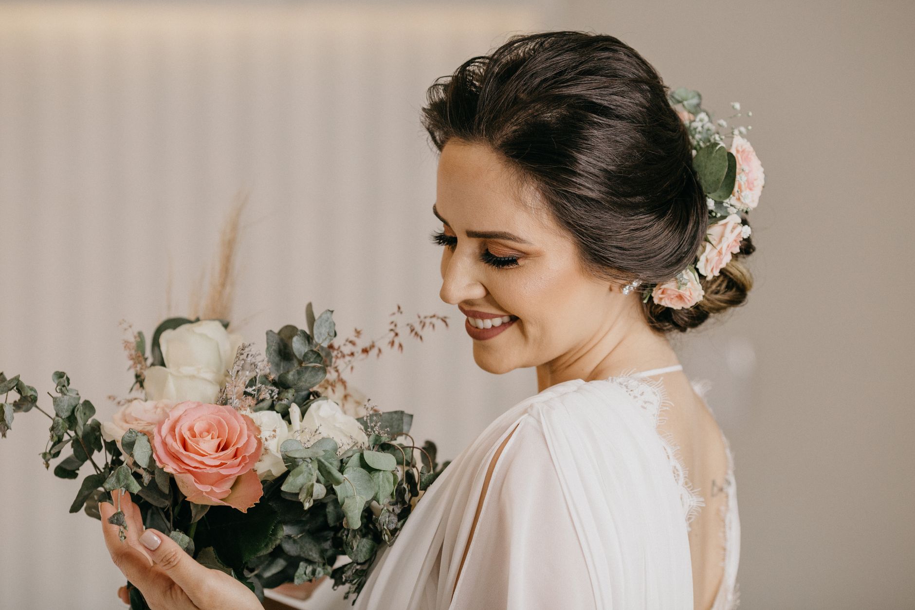 Seorang pengantin dalam gaun putih memegang buket, tersenyum dengan gaya rambut updo yang elegan.