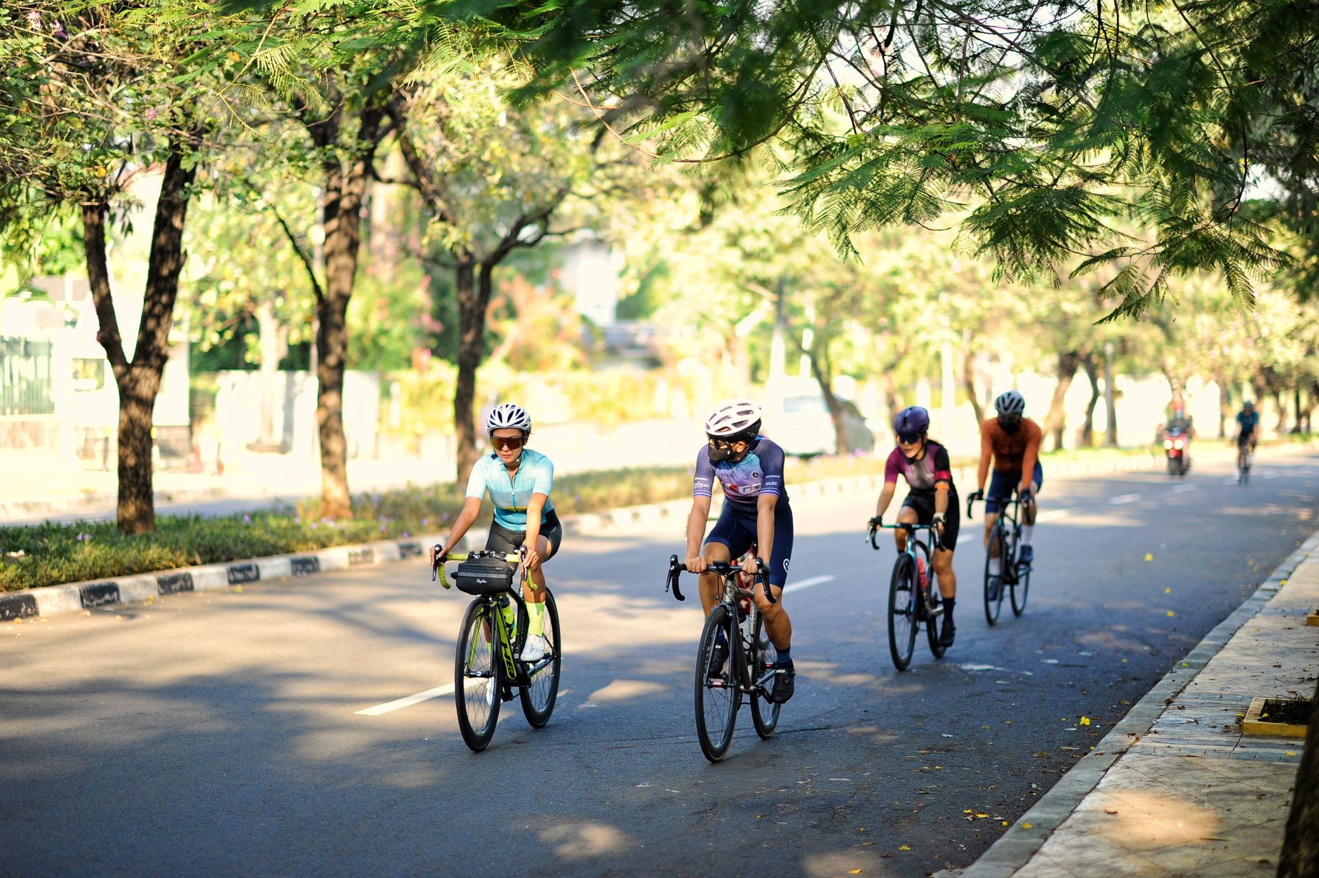Pengendara sepeda menikmati perjalanan cerah melalui jalan-jalan berdaun di Jakarta, Indonesia.