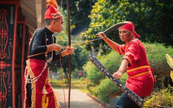 Dua pria terlibat dalam tarian prajurit tradisional Indonesia, menampilkan pakaian budaya dan senjata upacara.