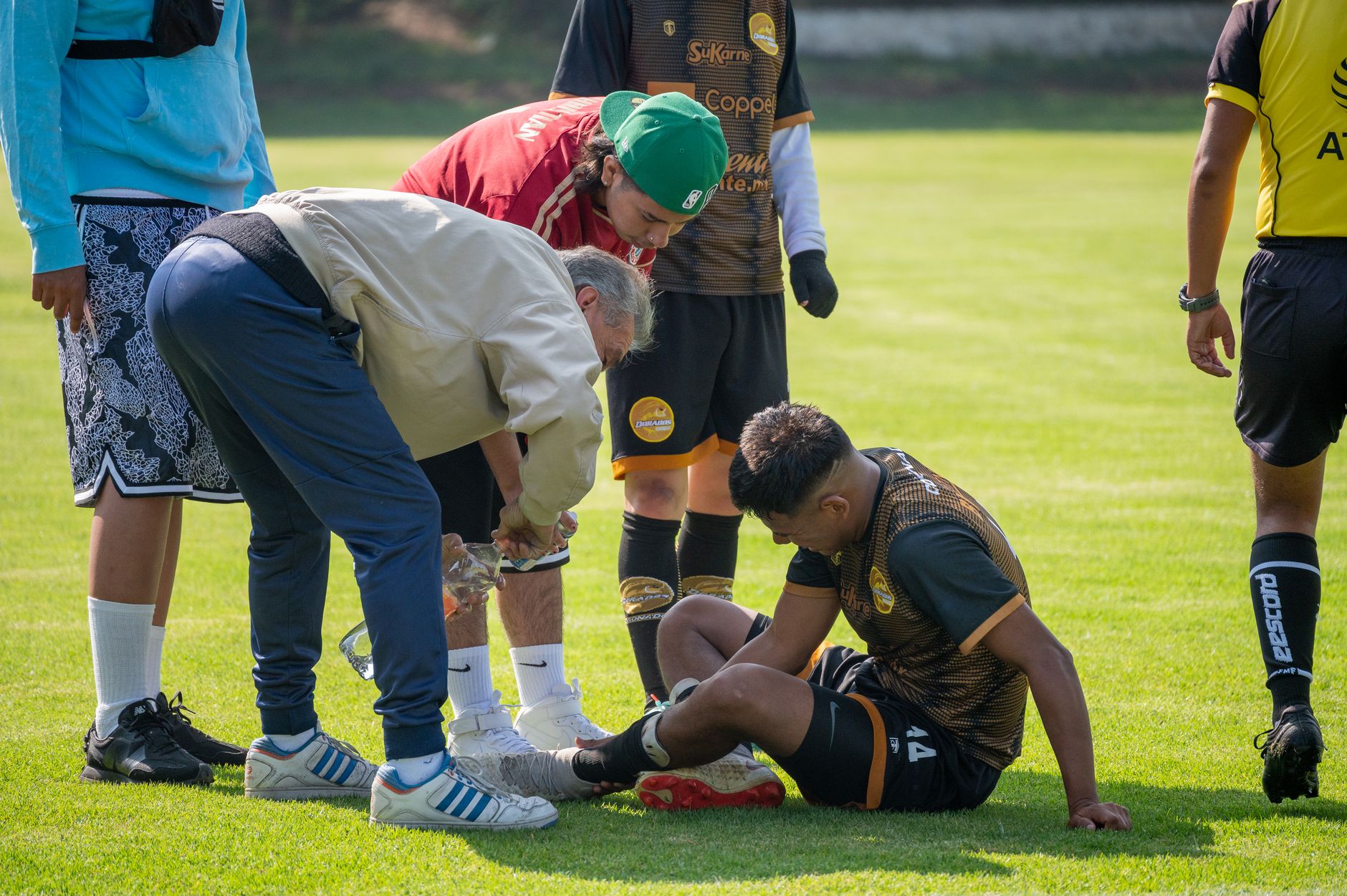 Pemain sepak bola cedera menerima perhatian medis di lapangan selama pertandingan.