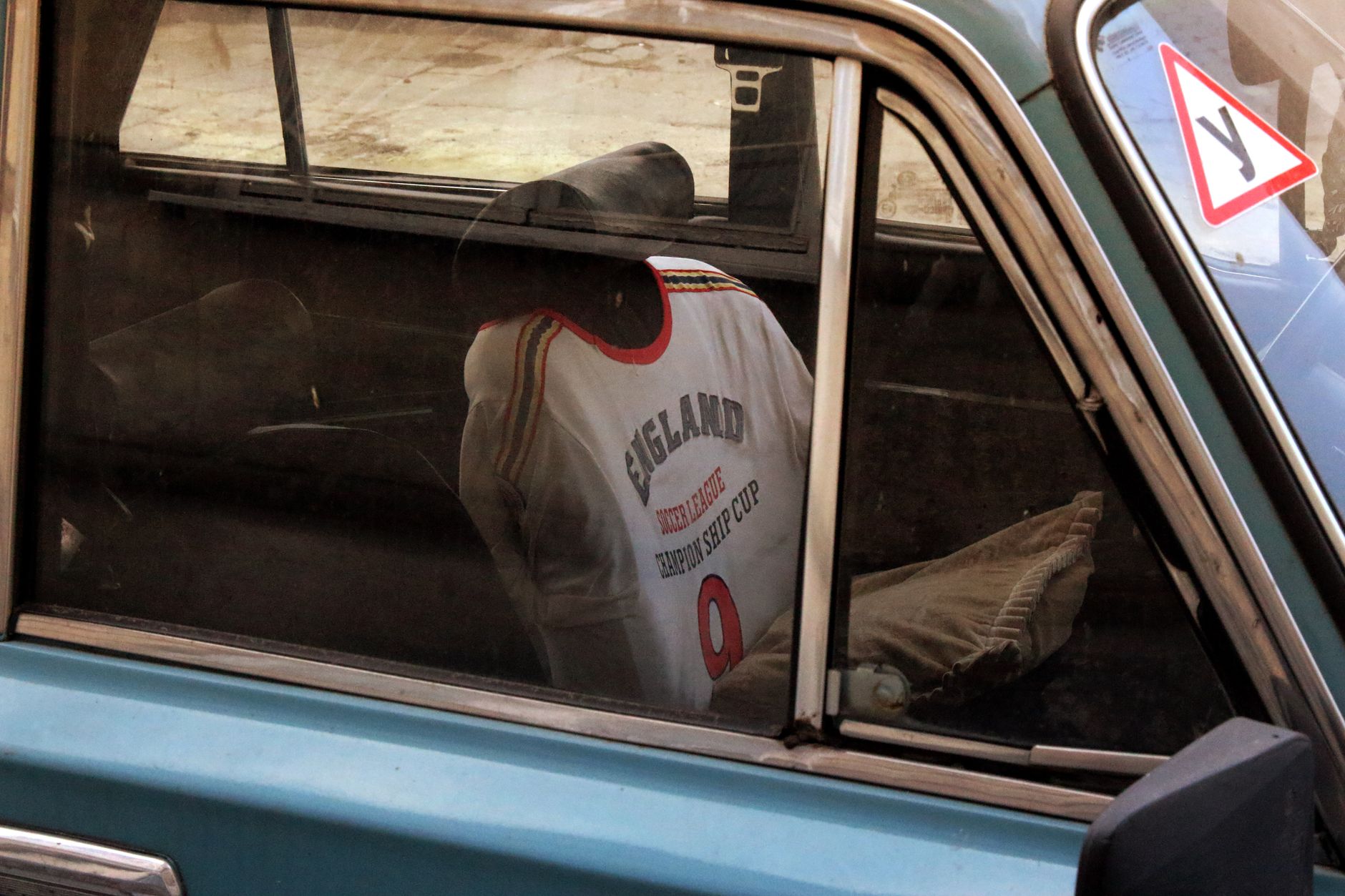 Refleksi jersey sepak bola Inggris di jendela mobil vintage. Diabadikan di Lwów, Ukraina.