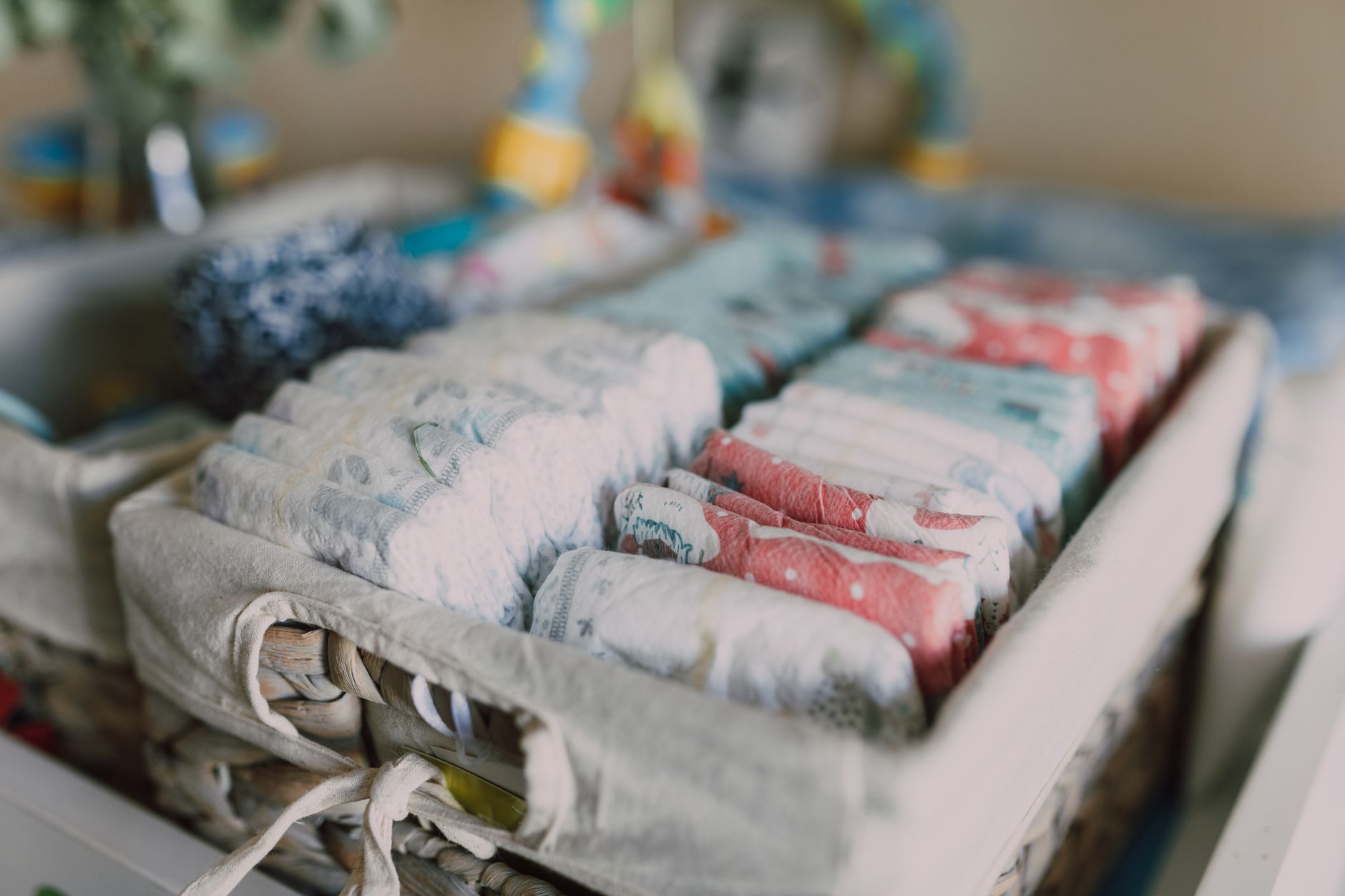 Close-up popok bayi berwarna yang tertata rapi dalam keranjang anyaman, ideal untuk organisasi ruang bayi.