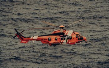 Helikopter penyelamat oranye terbang di atas ombak lautan, melaksanakan operasi darurat.
