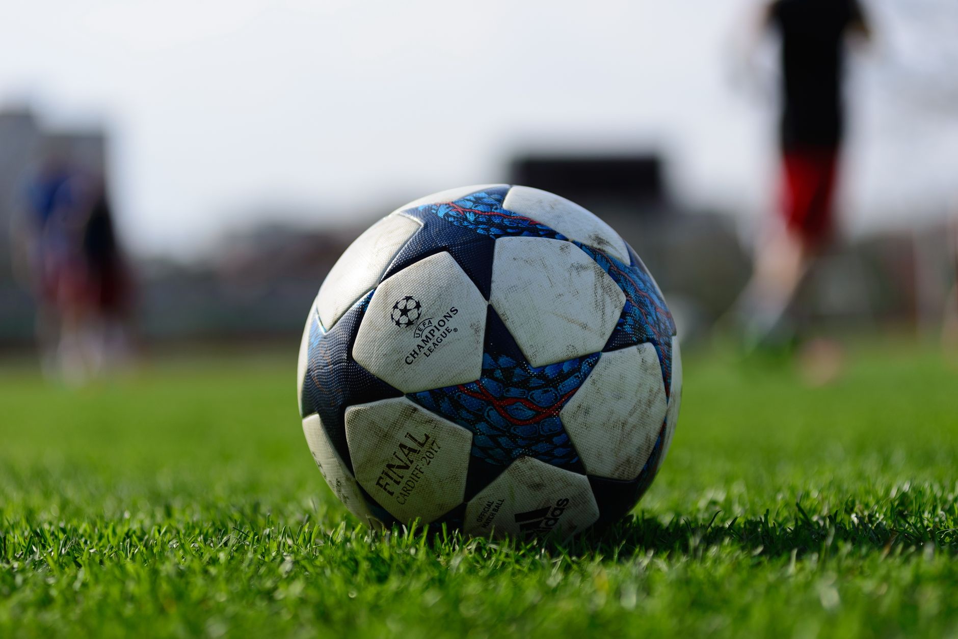 Fokus pada bola sepak yang tergeletak di lapangan olahraga hijau cerah di bawah sinar matahari.