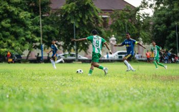 Pertandingan sepak bola dinamis yang dimainkan di lapangan berumput dengan para pemain yang antusias beraksi.