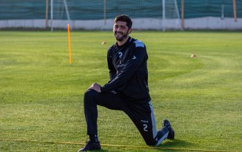 Pemain sepak bola mengenakan pakaian latihan yang melakukan latihan pemanasan di lapangan rumput.