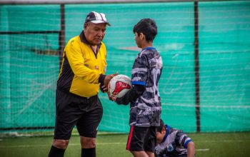 Seorang pelatih dewasa dan pemain muda selama sesi latihan sepak bola di luar ruangan di Chili.