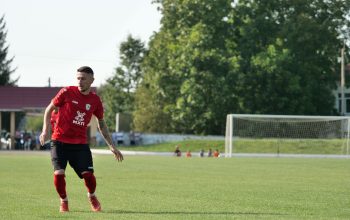Seorang pemain sepak bola mengenakan seragam merah di hari yang cerah, siap untuk melakukannya di lapangan.
