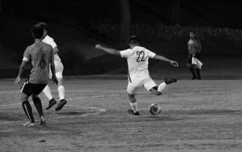 Foto hitam putih pemain sepak bola yang berlaga dalam pertandingan malam, menampilkan aksi dan keterampilan yang intens.