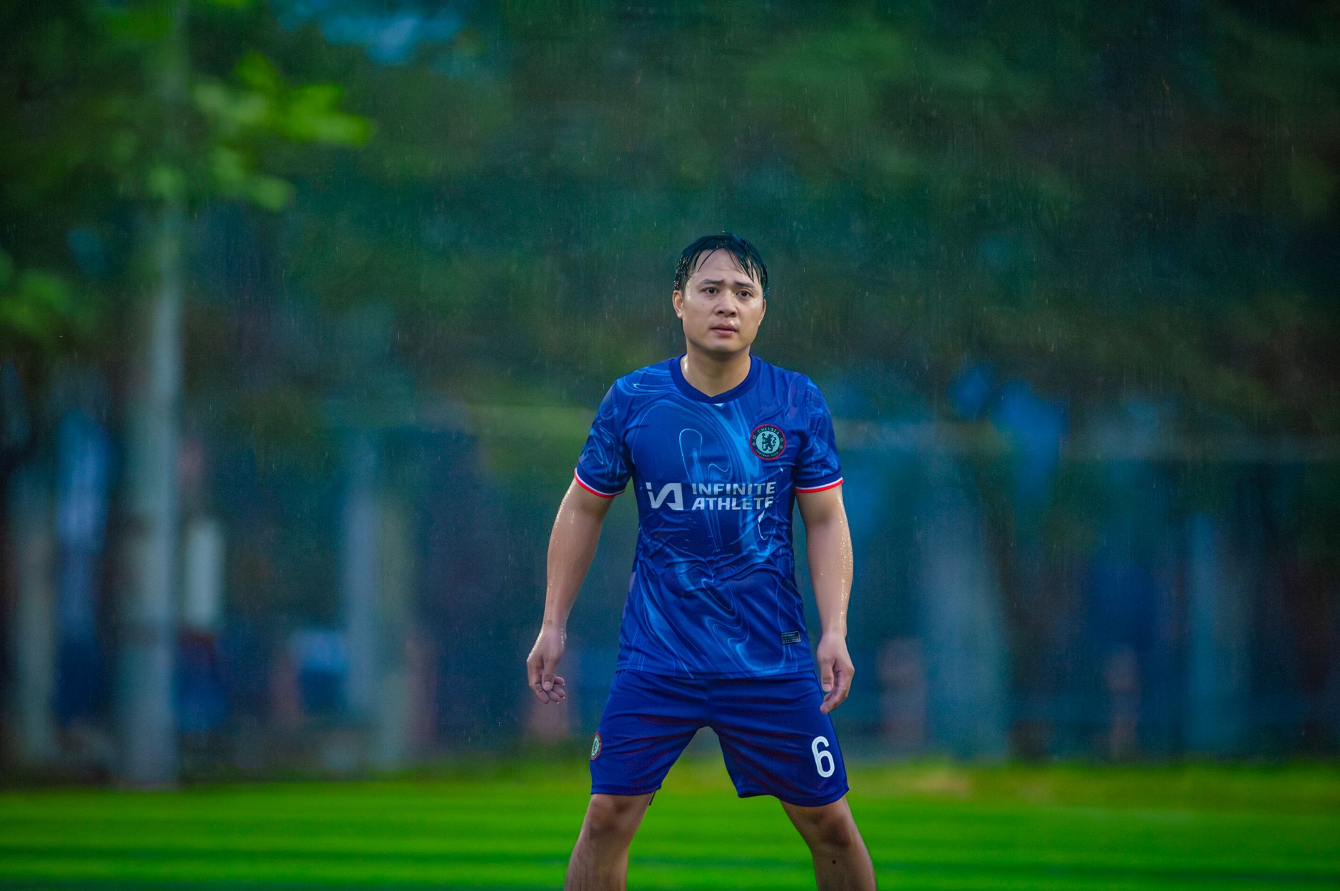 Foto dinamis seorang pemain sepak bola yang sedang beraksi di lapangan hujan di Hanoi, Vietnam.