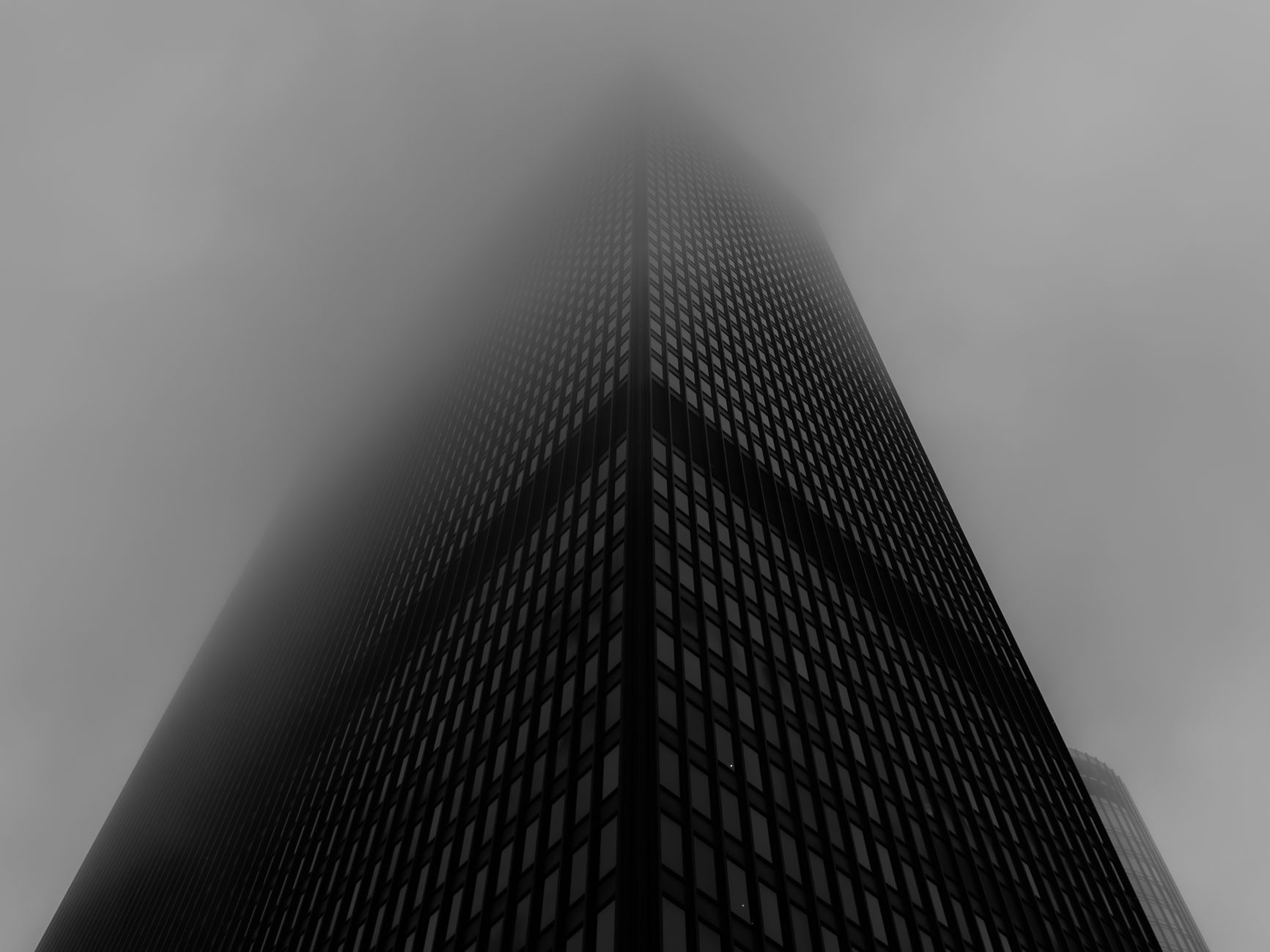 Sebuah gedung pencakar langit menjulang tinggi di Chicago yang diselimuti kabut, diabadikan dalam warna hitam putih yang penuh nuansa.