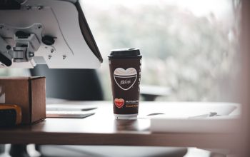 Cangkir kopi bermerek McCafe di meja kantor modern, menciptakan suasana kerja yang santai.