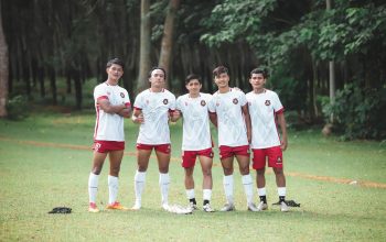 Sekel pemain sepak bola muda berpose dalam seragam tim di lapangan hijau yang subur. Pengaturan olahraga luar ruangan.