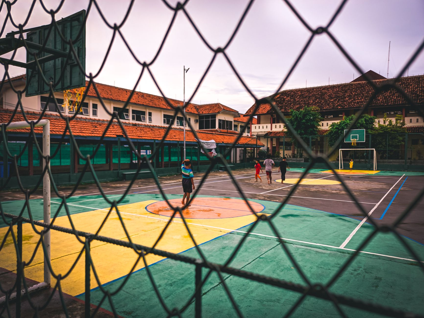 Orang-orang bermain di lapangan basket luar ruangan yang dikelilingi oleh pagar jaring.