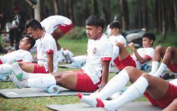 Pemain sepak bola dalam sesi latihan melakukan peregangan di lapangan di Jakarta.