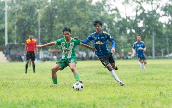 Para pemain terlibat dalam pertandingan sepak bola kompetitif di hari yang hujan.