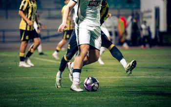 Gambar close-up para pemain sepak bola yang sedang beraksi selama pertandingan di stadion terbuka.