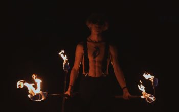 Seorang pria yang memegang obor menyala, menampilkan pertunjukan api dramatis dalam kegelapan.