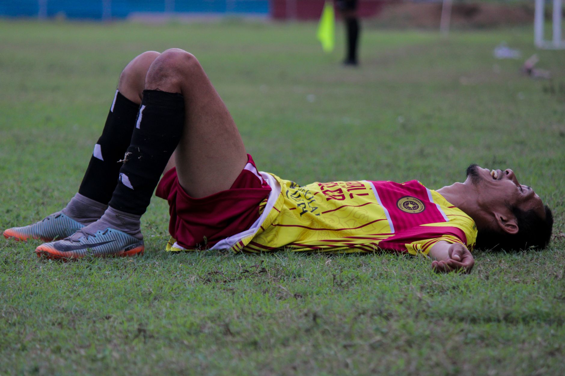 Seorang pemain sepak bola yang lelah berbaring di lapangan rumput setelah pertandingan yang intens.