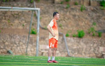 Seorang pria mengenakan pakaian olahraga berdiri di lapangan sepak bola pada siang hari.