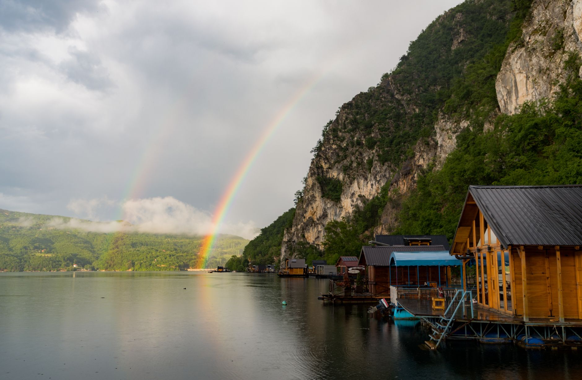 Pelangi ganda yang menakjubkan di atas danau yang tenang dengan rumah kayu di Перућац, Serbia.