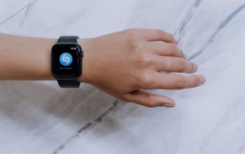 Close-up smartwatch di pergelangan tangan yang menampilkan aplikasi identifikasi musik dengan latar belakang marmer.