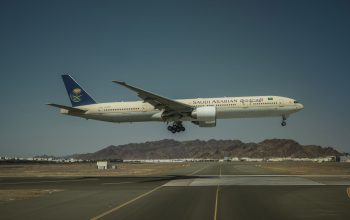 Sebuah pesawat Boeing 777 milik Saudi Arabian Airlines mendarat di landasan pacu dengan latar belakang pegunungan.