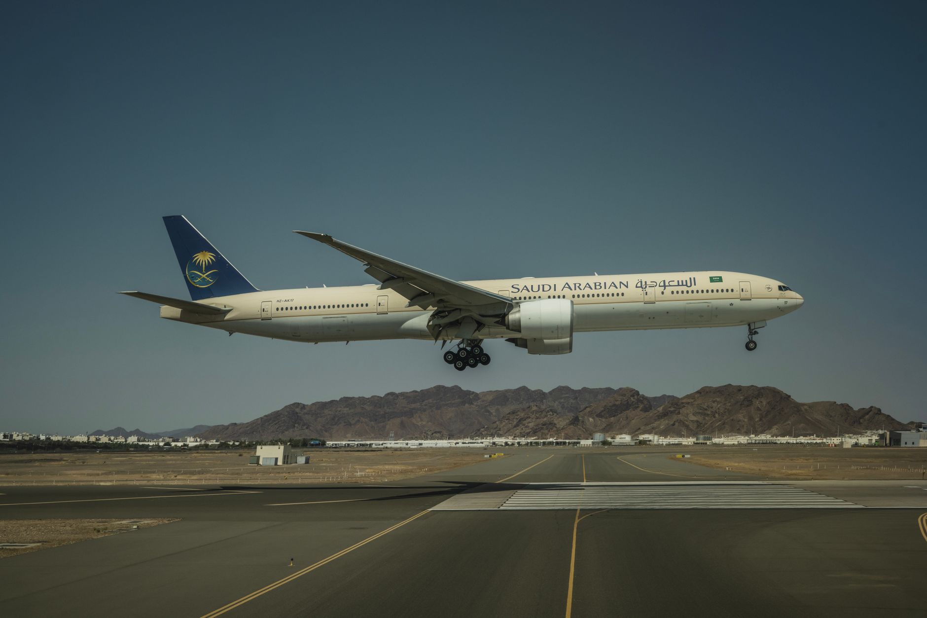 Sebuah pesawat Boeing 777 milik Saudi Arabian Airlines mendarat di landasan pacu dengan latar belakang pegunungan.