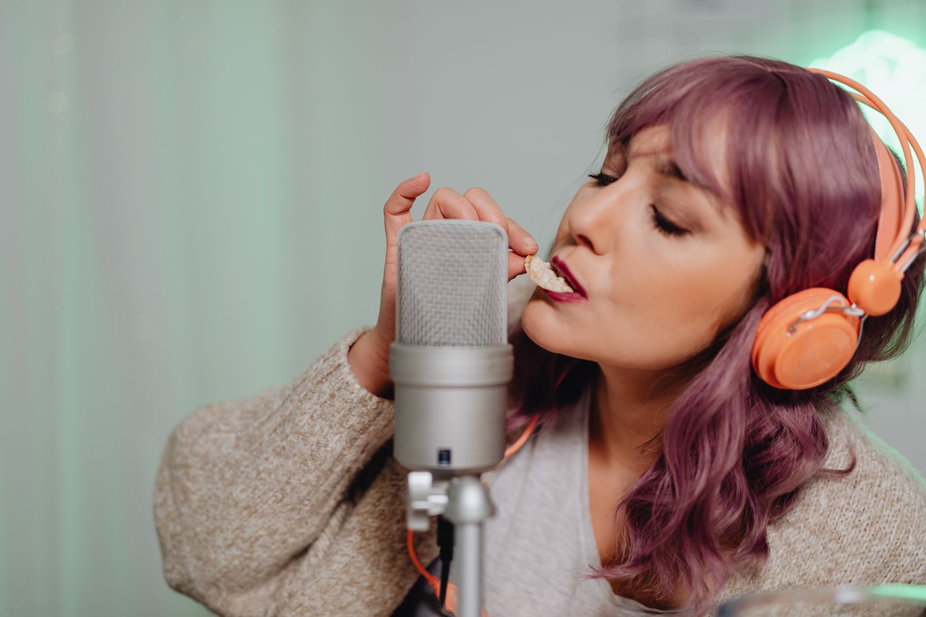 Wanita muda yang merekam konten ASMR dengan mikrofon dan headphone di dalam ruangan.