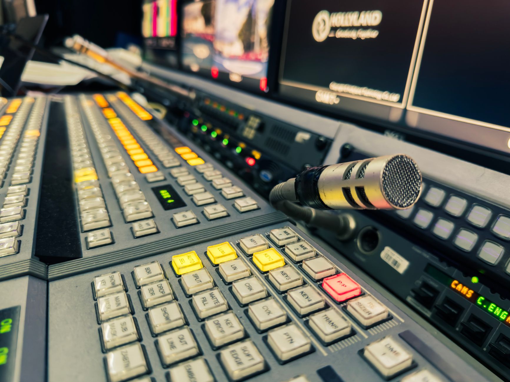 Tampilan detail panel kontrol studio penyiaran dengan mikrofon dan beberapa layar.